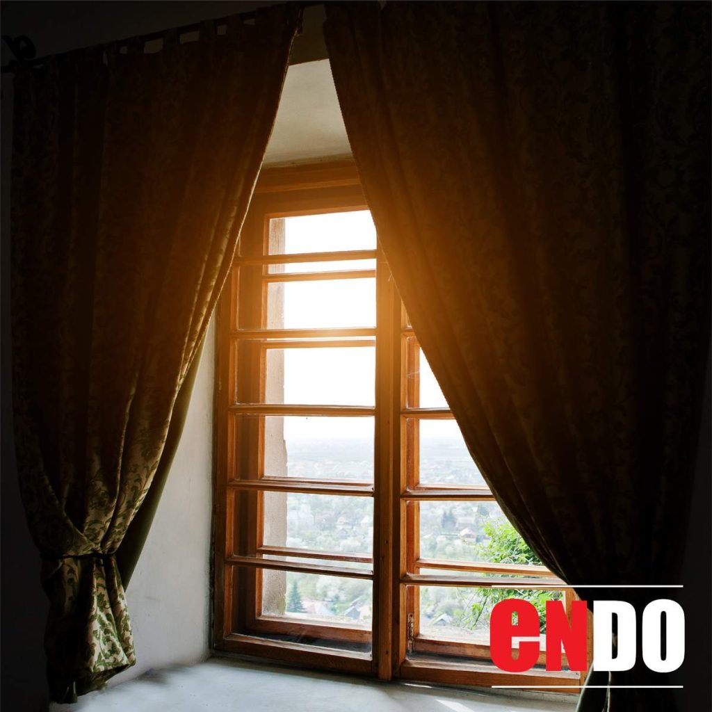 Dark patterned day and night curtains providing blackout beside a sunset-lit window
