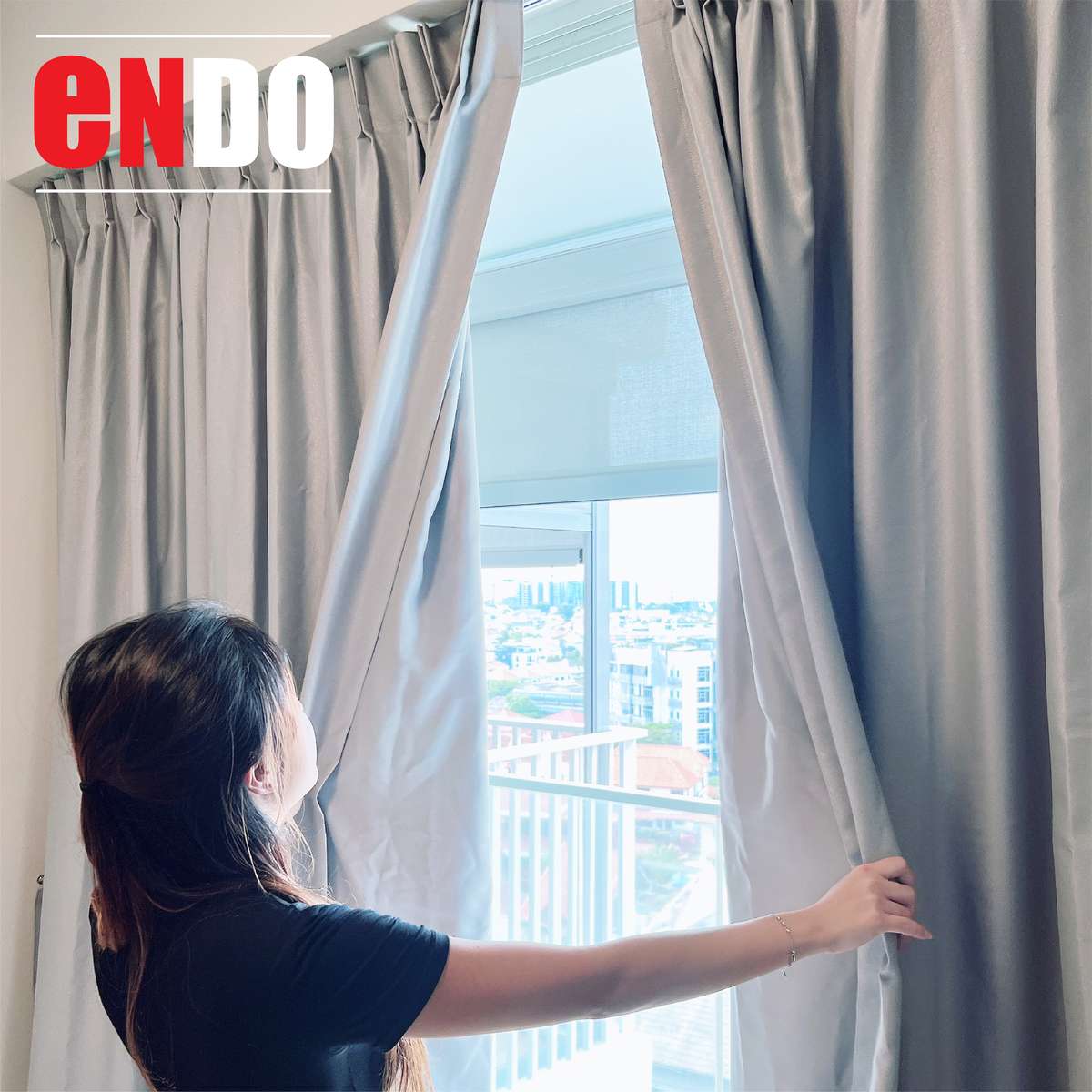 Woman opening brown curtains to reveal a roller blind and city view