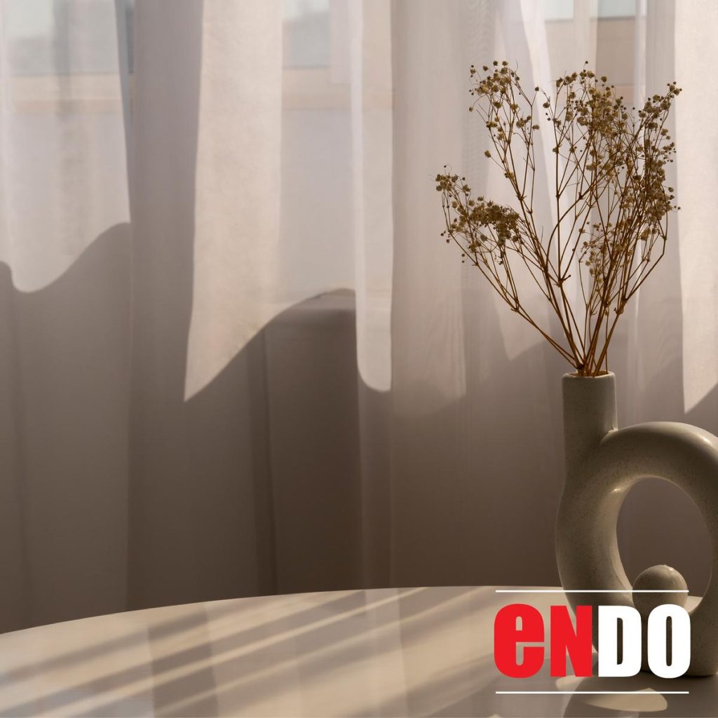 Sheer day curtain behind a vase of dried flowers on a table