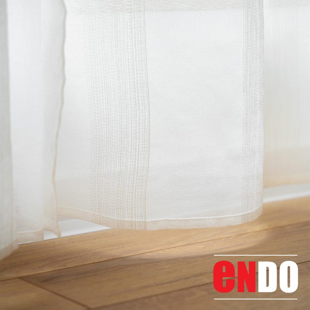 Close-up of sheer day curtain hem against a wooden floor