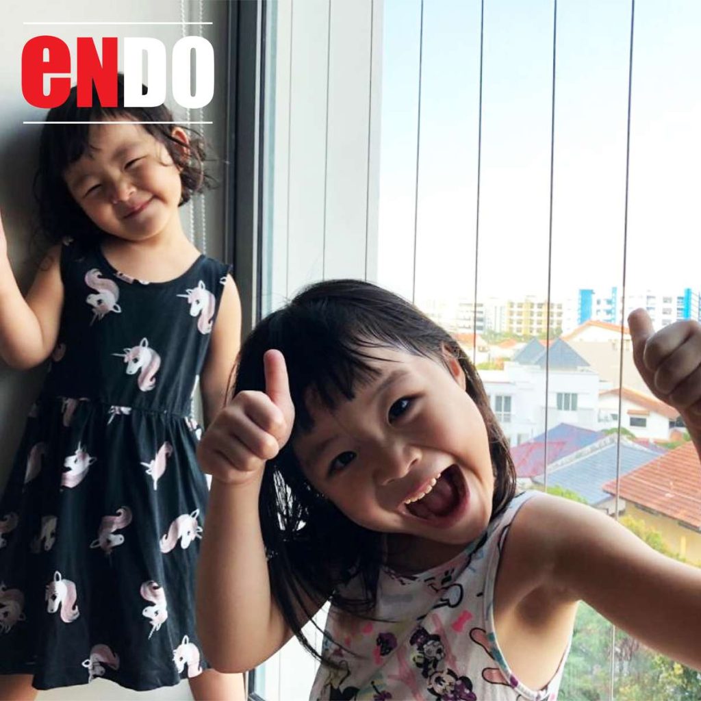 Two young children giving thumbs up beside an invisible safety grille installed on a window