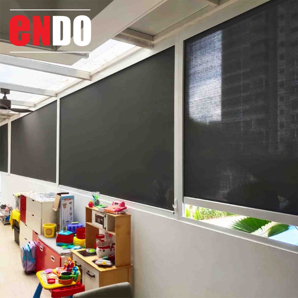 Row of dark mesh zip blinds installed along a covered patio used as a children's playroom, with a ceiling fan overhead